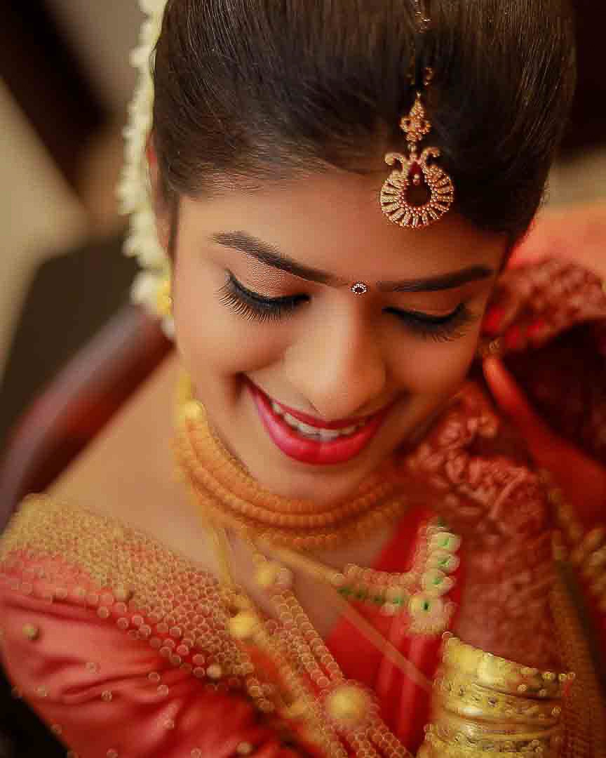 kerala bride close up shot she is in a red saree and full of ornaments, the photograph is taken during her kerala wedding photography session very artistically